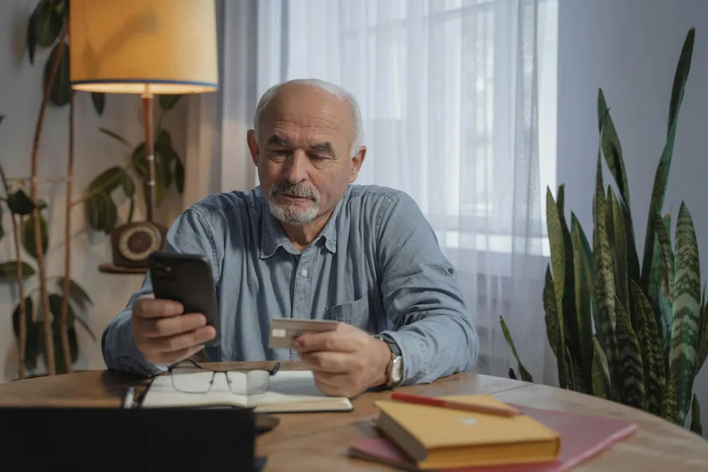 Older man at his table at home, talking on his mobile phone with paperwork beside him